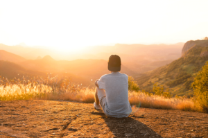 a young man takes care of his mental health by sitting in nature and thinking or meditating