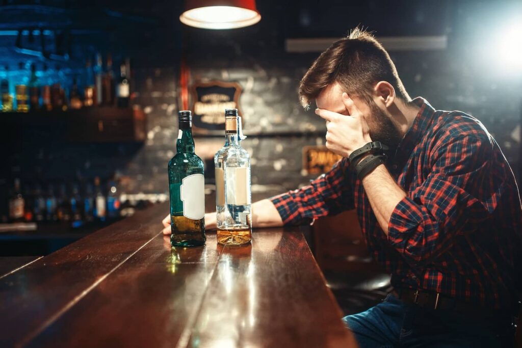 An alcoholic sitting at a bar with two bottles