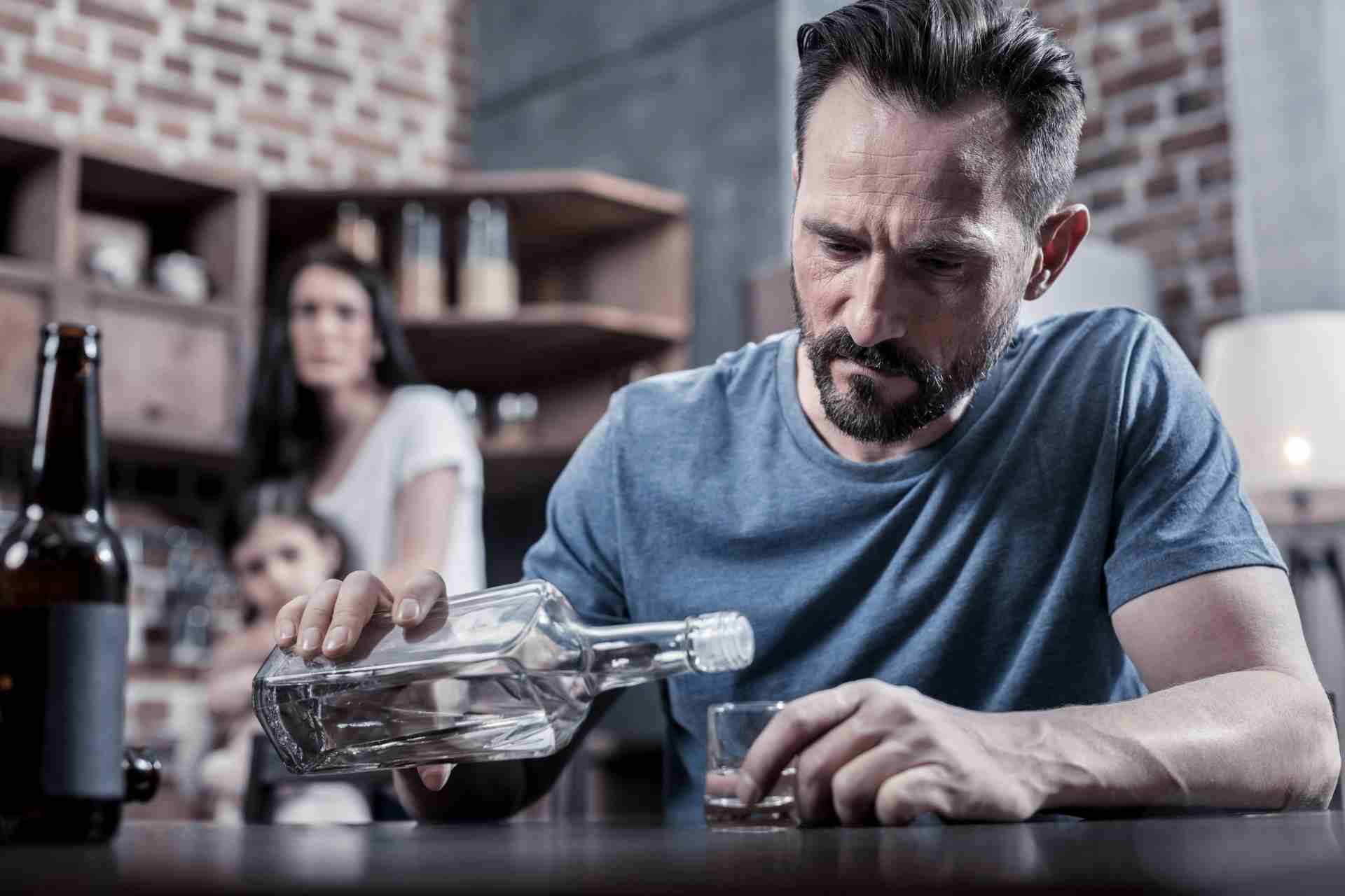 Man pouring alcohol while family looks on in the background, showing signs of alcohol addiction