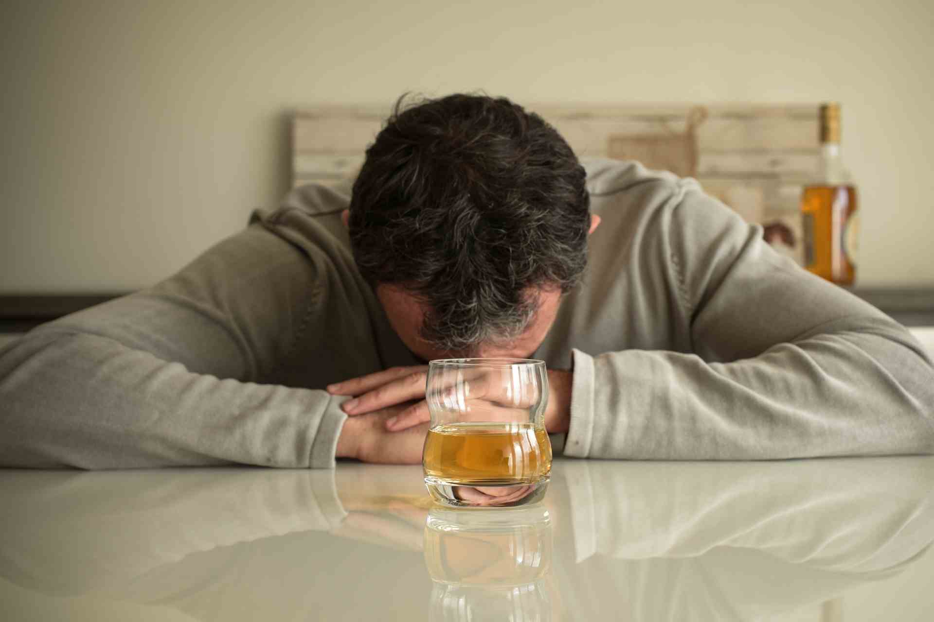 Man leaning on table with glass of alcohol showing struggle with drinking problem