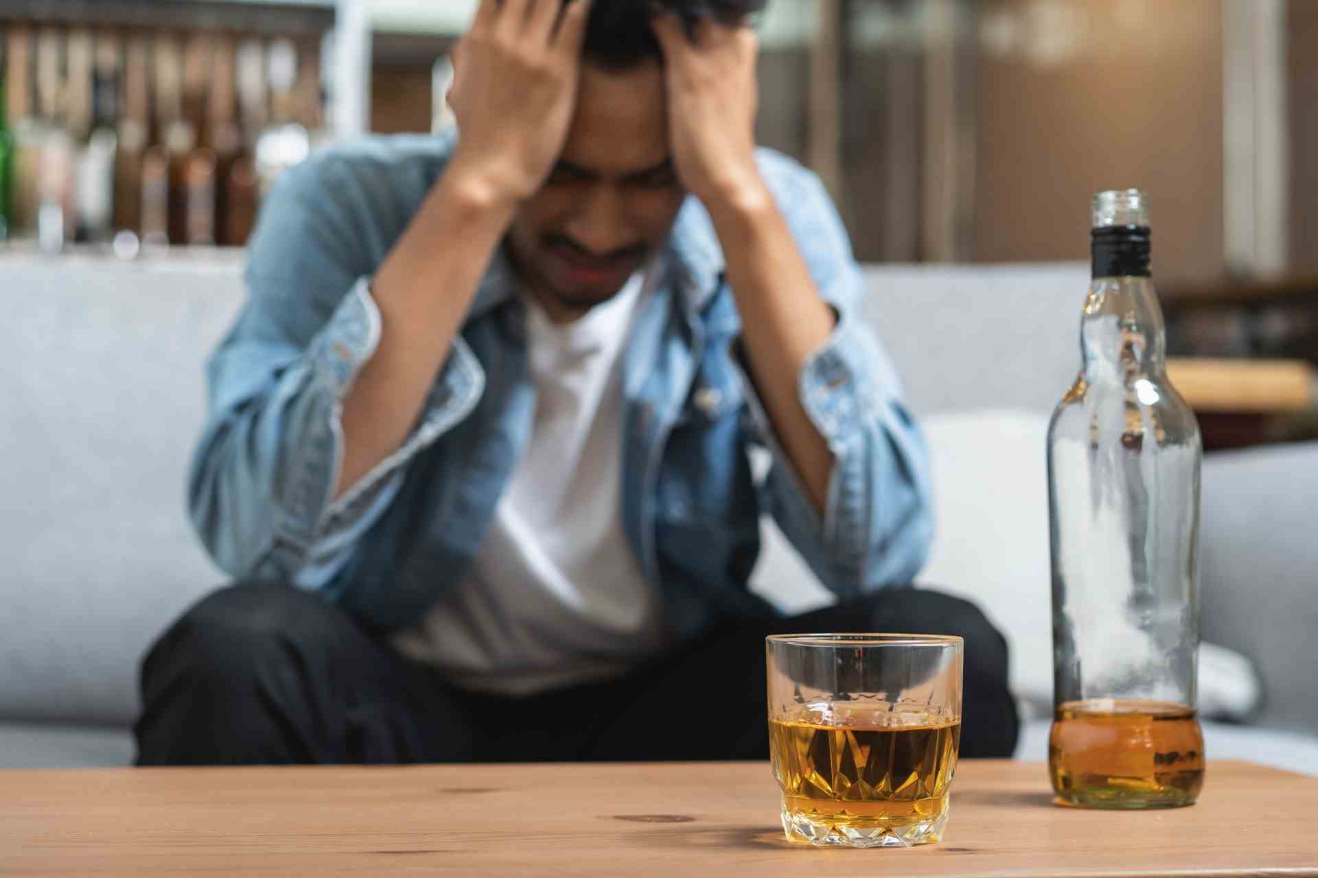 Man holding his head with alcohol bottle and glass showing struggle with alcohol addiction and withdrawal