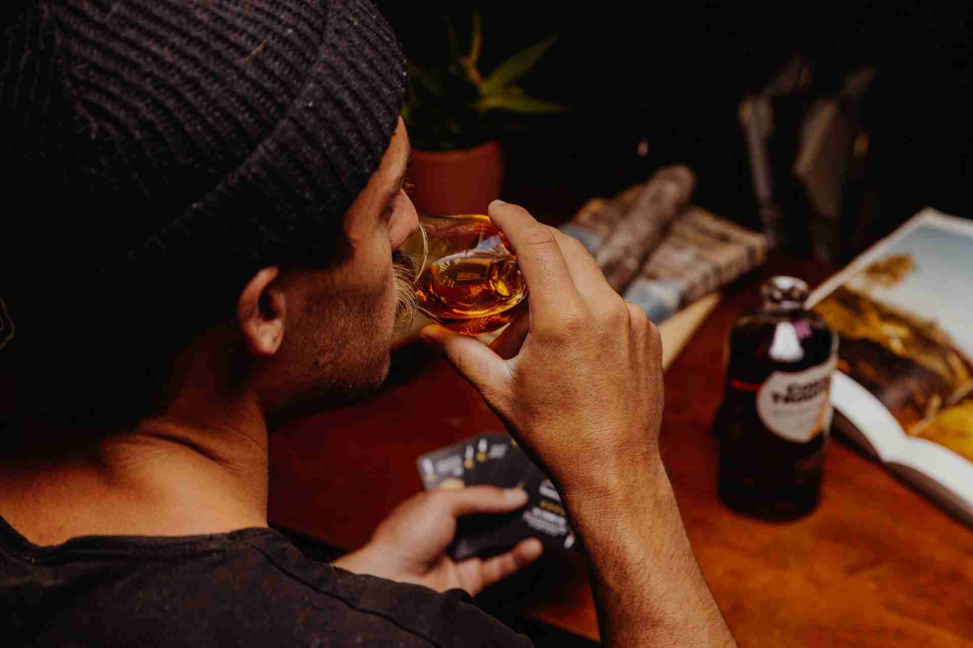 Man drinking whiskey indoors, representing alcohol use disorder and unhealthy drinking habits.