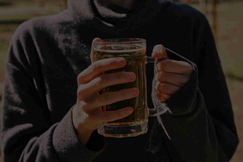 Person holding a glass of beer outdoors, representing early signs of alcoholism and habitual alcohol use.
