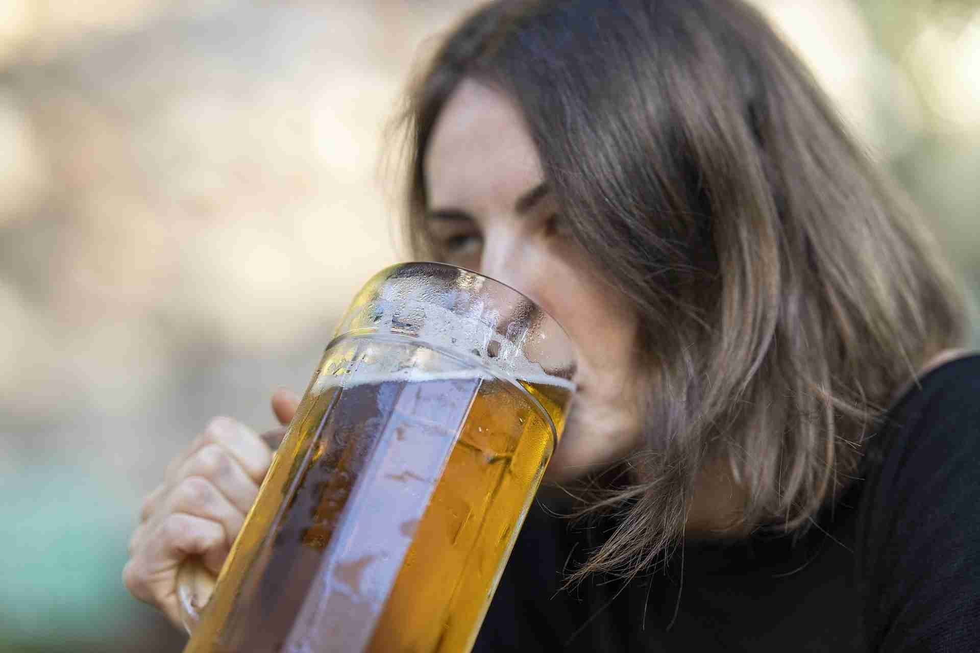 Woman drinking a large glass of beer, representing alcohol dependence and excessive drinking habits.
