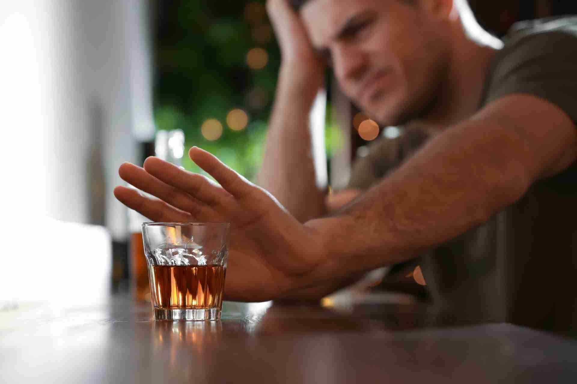 Man refusing a glass of alcohol while beginning recovery from alcohol dependence